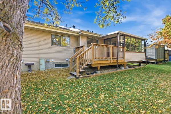 Back exterior of the duplex with a wooden deck, stairs leading down, and a screened-in sunroom addition. - 263 Oeming Rd Nw, Edmonton