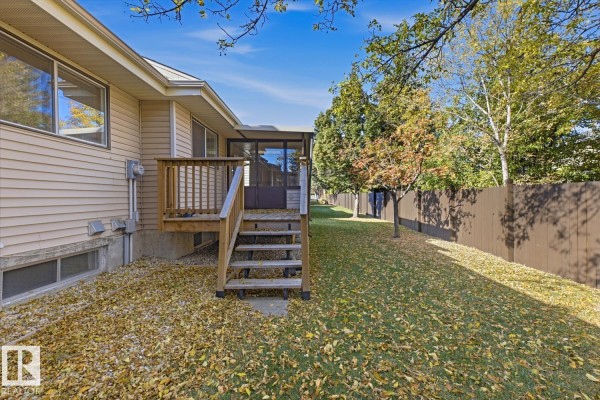 Side view of the duplex backyard featuring a lawn with fallen leaves, a wooden deck, and a screened-in room. - 263 Oeming Rd Nw, Edmonton