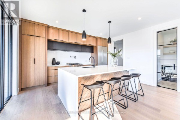 Contemporary kitchen with light wood cabinets, white island with waterfall edge, and black pendant lights. - 263 Silver Maple Circle, Thames Centre