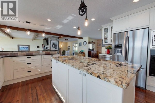 Kitchen island with granite countertop, white cabinets, and stainless steel appliances. Dark wood floors visible. - 2631 Johnson Road, Fraser Lake