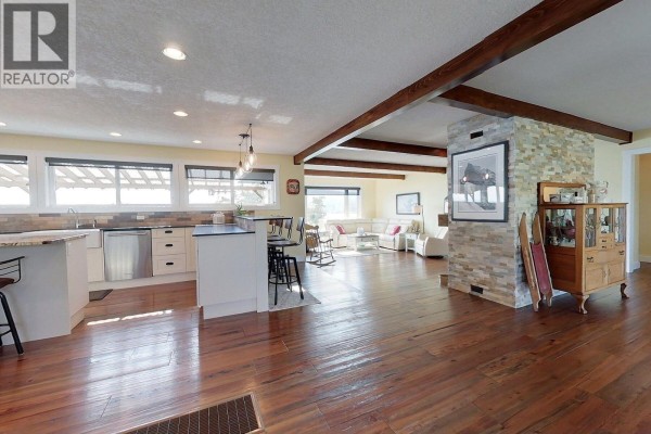 Open concept living area with a stone fireplace, kitchen island, bar stools, and a sofa in the background. - 2631 Johnson Road, Fraser Lake