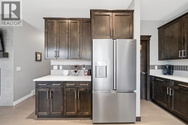 Stainless steel refrigerator and dark wood cabinets in a contemporary kitchen with white quartz counters. - 2632 Ravenslea Gardens Se, Airdrie
