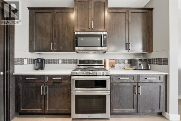 Stainless steel gas range with double ovens and dark wood cabinets in a modern kitchen. - 2632 Ravenslea Gardens Se, Airdrie