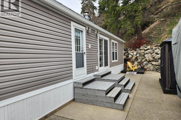 Side view of mobile home with gray steps leading to a doorway and sliding glass doors. - 2633 Squilax-anglemont Road Unit# 83, Lee Creek