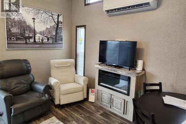 Living room with two armchairs, a television on an electric fireplace stand, and a small dining table. - 2633 Squilax-anglemont Road Unit# 83, Lee Creek