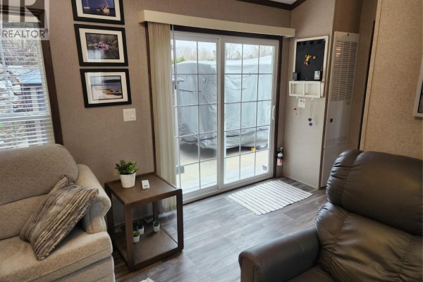 Living room area with sliding glass doors showing a covered trailer, and adjacent recliner chair. - 2633 Squilax-anglemont Road Unit# 83, Lee Creek