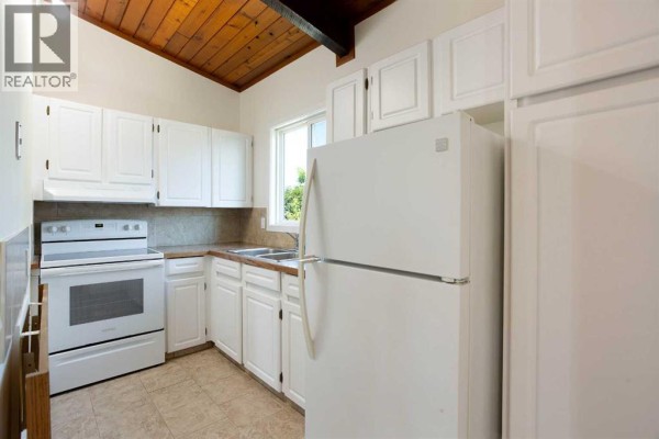 White kitchen cabinets, white appliances including a refrigerator and oven, and a beige tiled floor. - 2634 Oakmoor Drive Sw, Calgary