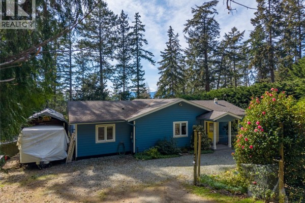 Blue single-story house with white trim, yellow door, and covered boat storage. - 2635 Shoal Rd, Pender Island