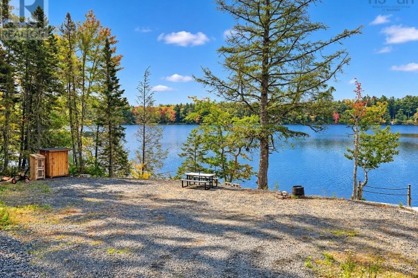 Gravel lot with a picnic table and a small wooden shed overlooks a calm blue lake. - 264 Beaver Dam Trail, Labelle