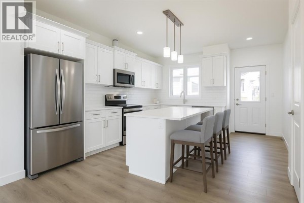 Kitchen with stainless steel appliances, white cabinetry, and island seating - 264 Clearview Court, Chestermere