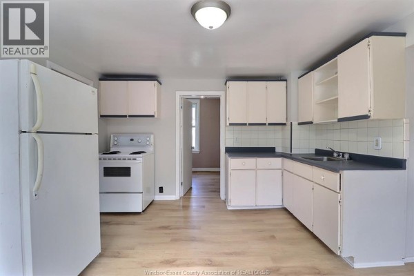 Kitchen with white appliances, white cabinets, dark countertops, and light wood-look flooring. - 2640 Whelpton, Windsor