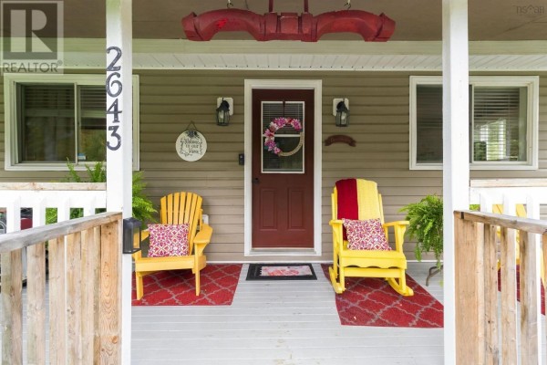 Close-up of a covered porch with two yellow Adirondack chairs, a red door, and a wreath. - 2643 Highway 210, Chelsea