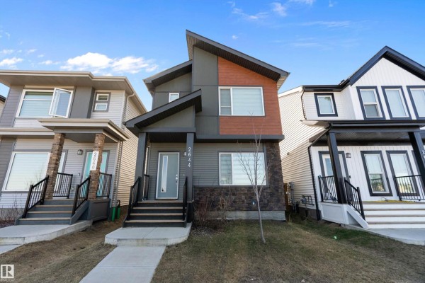 Open-concept living area with white walls, a fireplace with a mounted TV, stainless steel appliances, and light wood flooring. - 2644 192 St Nw, Edmonton