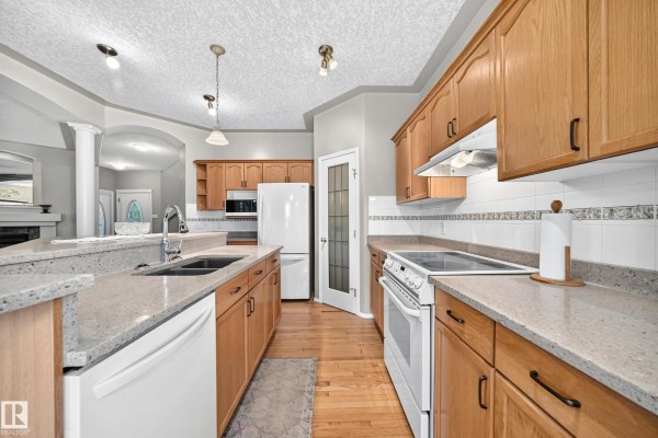 Kitchen island with sink, dishwasher, light wood cabinets, white appliances, and tiled backsplash. - 265 Dunvegan Rd Nw, Edmonton