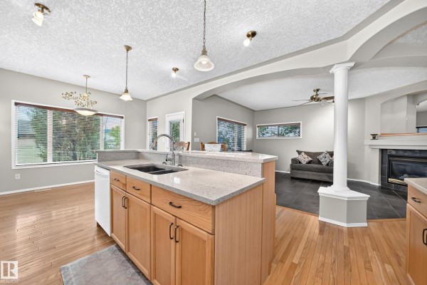 Open concept kitchen and living area with a fireplace, large windows, and pendant lights. - 265 Dunvegan Rd Nw, Edmonton