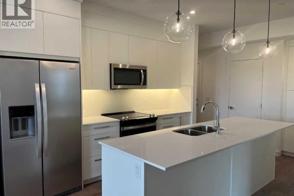 Modern kitchen with stainless steel appliances, a white island, and pendant lights, wood flooring. - 265 Wolf Willow Blvd Boulevard Se, Calgary
