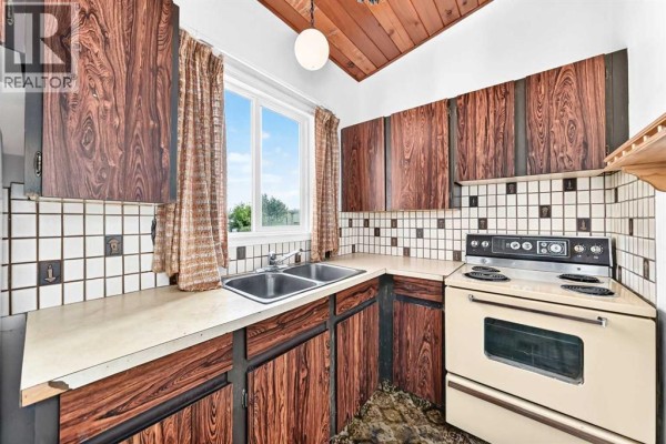 Corner view of a kitchen with wood-paneled cabinets, tiled backsplash, and a beige stove. - 2652 Oakmoor Drive Sw, Calgary