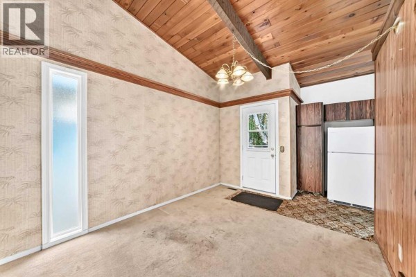 Interior room with beige carpet, patterned wallpaper, and a white door leading outside. - 2652 Oakmoor Drive Sw, Calgary