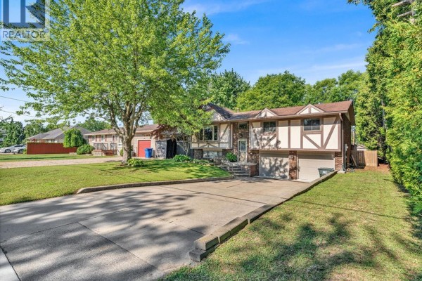 Wide angle view of the house from the street showing the driveway, lawn, surrounding trees, and neighboring properties. - 2653 Concession Rd 12, Tecumseh