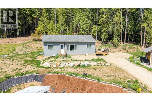 Close-up of the gray house featuring a front porch and landscaped yard. - 2655 Cowan Road, Sicamous