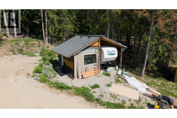 Aerial view of the property showing the house, outbuilding, and surrounding forested area. - 2655 Cowan Road, Sicamous