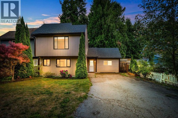 Front view of the beige duplex with manicured trees and a white picket fence. - 2655 Rhum & Eigg Drive, Squamish