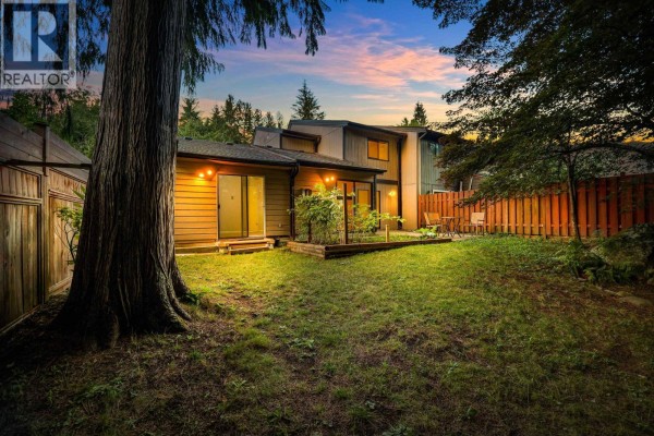 Backyard view of the duplex showing a large grassy area and mature trees. - 2655 Rhum & Eigg Drive, Squamish
