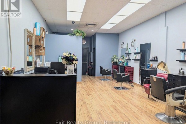 Interior view of a hair salon with light wood floors, blue walls, black chairs, mirrors, and a reception desk. - 266 Dundas Street E, Quinte West