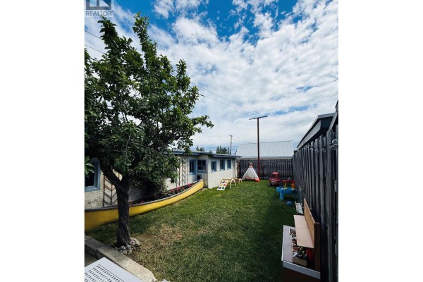Backyard with green grass, trees, a yellow canoe planter, children's play structures, and a wooden bench. - 266 Ritchie Street, Kimberley