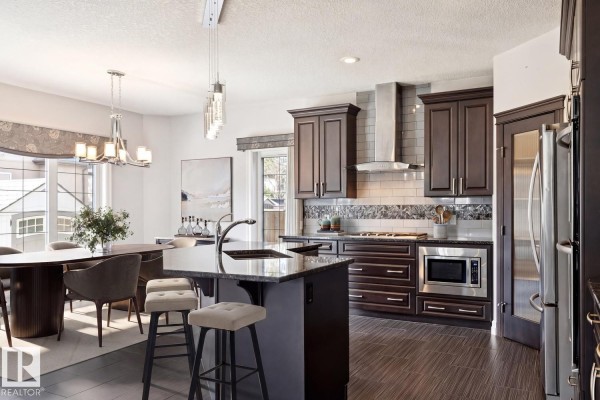 Kitchen and dining area with dark wood cabinets, granite countertops, stainless steel appliances, and island seating. - 2665 Watcher Wy Sw, Edmonton