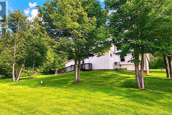 Rear view of the house showing a wooden deck and a sloped grassy yard with mature trees. - 2668 Rte 363, Saint Sauveur