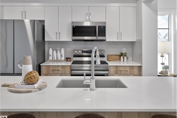 Modern kitchen with white cabinets, stainless steel appliances, and a large sink. - 267 Deer Valley Dr, Leduc