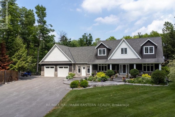 Front view of a spacious house with a covered porch, white trim, stone accents, and a large driveway. - 267 Edwina Drive, Trent Lakes