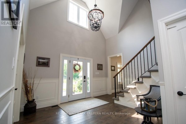 Foyer with vaulted ceiling, double front doors, staircase with dark banister, and hardwood floors. - 267 Edwina Drive, Trent Lakes