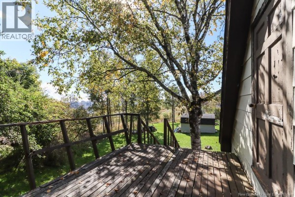 Wooden deck with railing overlooking a backyard with trees and distant buildings. - 267 Milford Road, Saint John