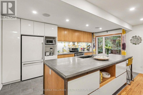 Kitchen with white and wood cabinets, concrete island with yellow stools, and window. - 267 St Laurent Boulevard, Ottawa