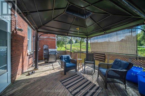 Covered patio with wicker chairs, a rug, a grill, and a view of green fields. - 2671 Champlain Street, Clarence Rockland