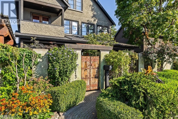 Close-up of a garden path with brick pavers leading to rustic wooden double doors and lush greenery. - 2673 Bath Street, Kelowna