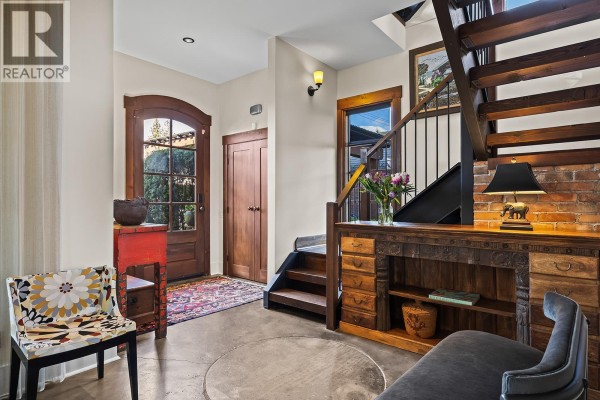 Entryway with wooden floors, a decorative chair, a console table, and a staircase with brick accent wall. - 2673 Bath Street, Kelowna
