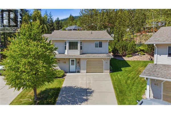 Aerial view of the front of a beige duplex with a single car garage and green lawn. - 2675 Pine Avenue Unit# 41, Lumby