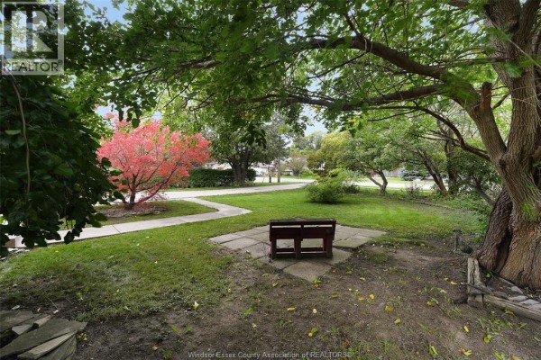 Outdoor seating area with a wooden bench on a flagstone patio, surrounded by trees and greenery. - 268 Broadway Street, Belle River