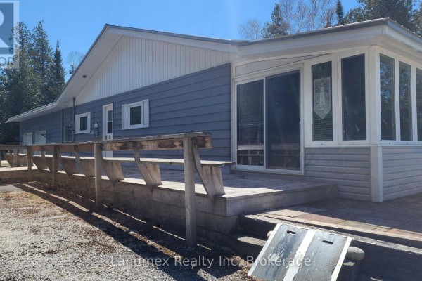 Deck with built-in wooden seating runs along the side of a light blue house with a sunroom. - 268 Dorcas Bay Road, Northern Bruce Peninsula