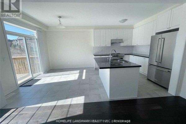 White kitchen cabinets, granite island, stainless steel refrigerator, and sliding glass doors to a deck. - 268 Silk Twist Drive, East Gwillimbury