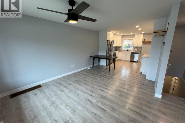 Kitchen with white cabinets, gray speckled backsplash, stainless steel appliances, and light wood laminate flooring. - 2680 75 Avenue Unit# B, Grand Forks