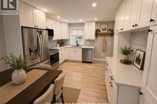 Corner view of the kitchen showcasing white cabinets, gray speckled backsplash, stainless steel appliances, and quartz countertops. - 2680 75 Avenue Unit# B, Grand Forks