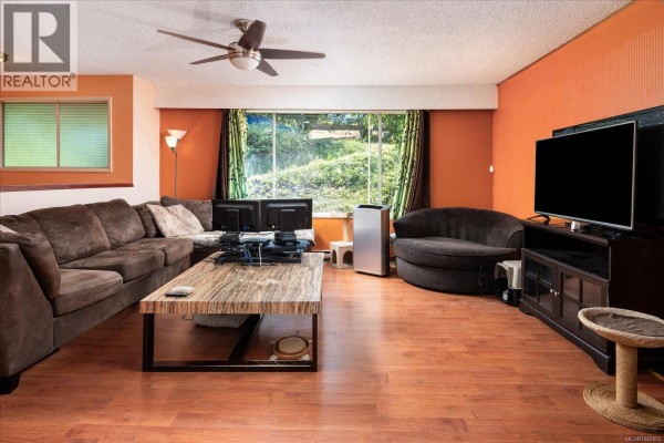 Living room with dark brown sectional sofa, wooden coffee table, and large window. - 2682 Beaver Creek Cres, Nanaimo