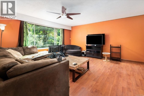 Living room with orange accent wall, sectional sofa, entertainment center, and hardwood floors. - 2682 Beaver Creek Cres, Nanaimo