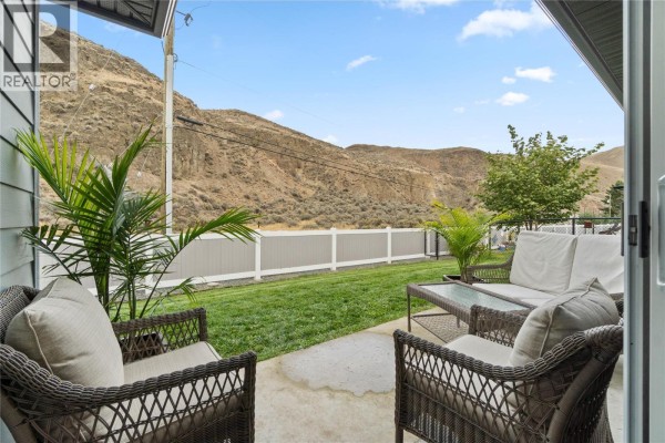 Backyard patio with wicker furniture, grass, fence, and a scenic view of arid hills. - 2683 Ord Road Unit# 148, Kamloops