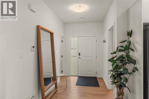 Interior hallway with white walls, hardwood floors, a large mirror, and a potted plant. - 2683 Ord Road Unit# 148, Kamloops