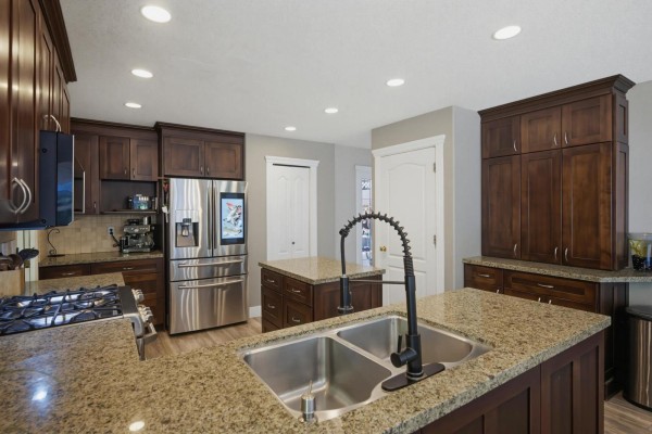 Kitchen view from the side showing dark wood cabinets, granite countertops, stainless steel appliances, and island. - 26860 24a Avenue, Langley